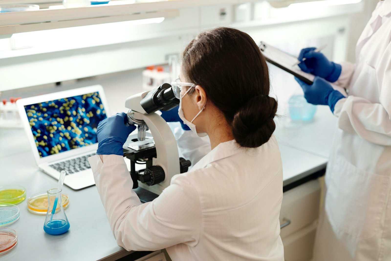 A female scientist in a lab coat examines samples under a microscope for research.